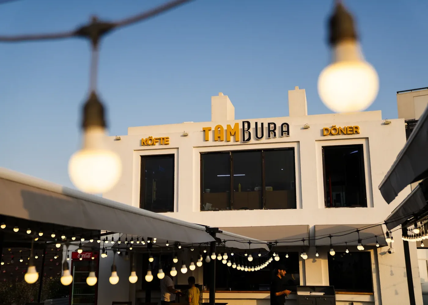 Фасад Tambura: вывески «Köfte» и «Döner», терраса с гирляндой
